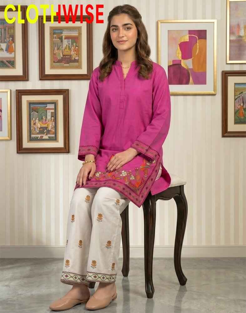 Woman wearing a pink kurta with white pants sitting on a chair in a room with framed pictures on the wall.