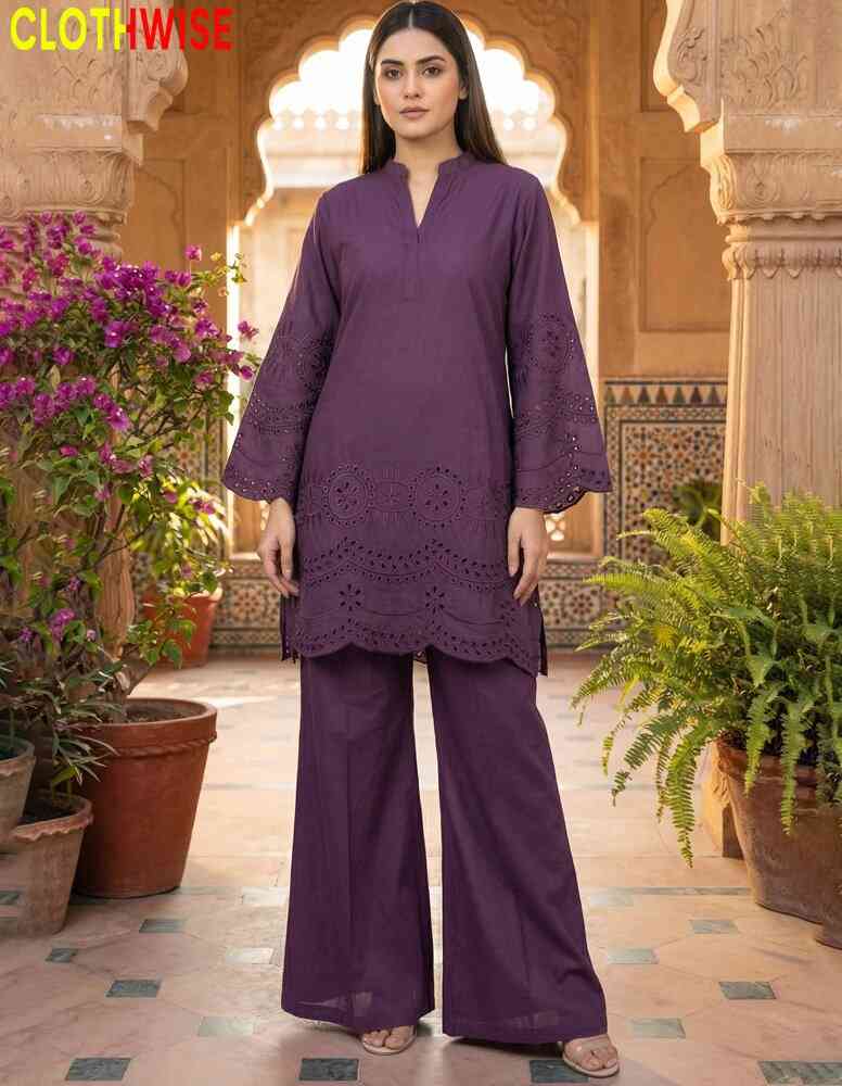 Woman wearing a purple outfit standing in an outdoor setting with plants and architecture.