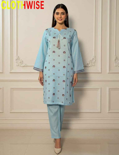Woman wearing a light blue kurta with floral patterns against a white paneled wall.