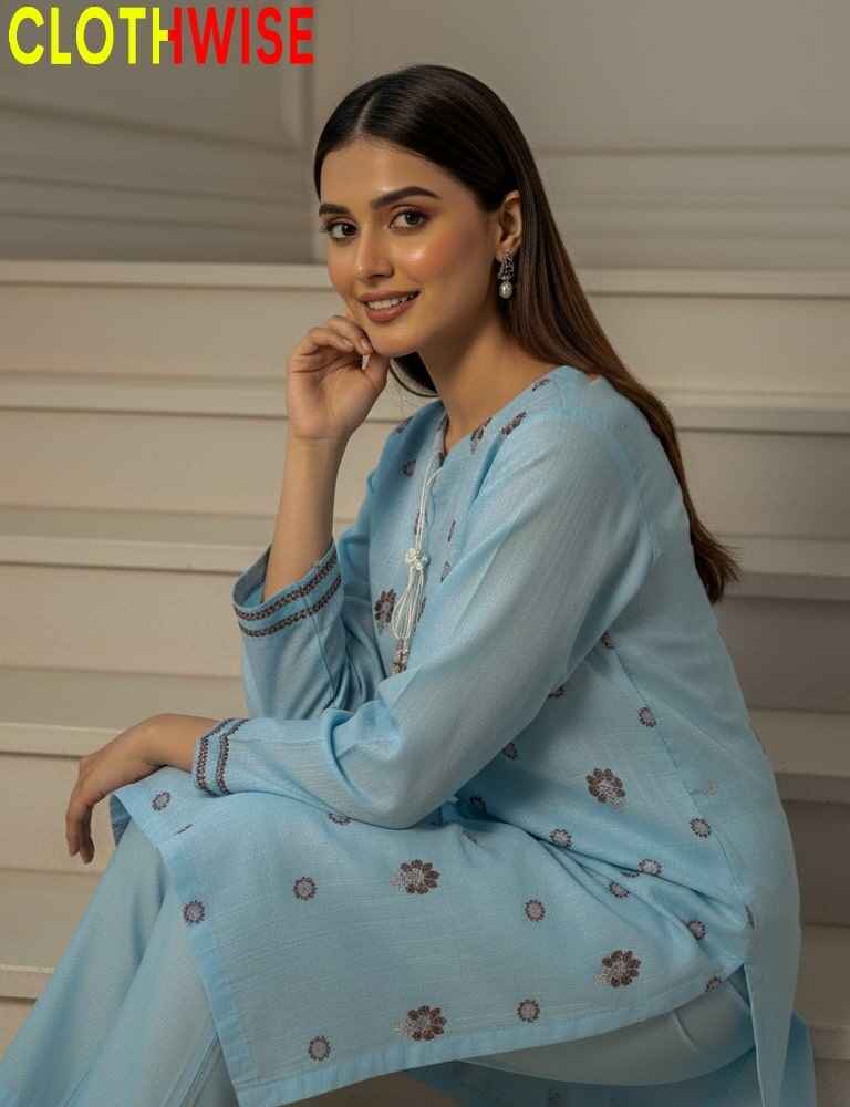 Woman wearing a light blue traditional outfit with floral patterns, sitting against a neutral background.