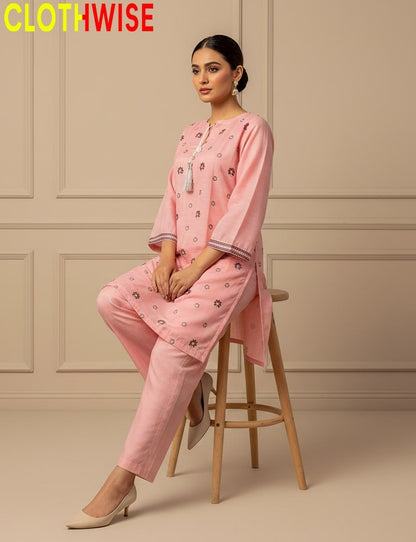 Woman wearing a pink outfit with floral patterns sitting on a stool against a beige wall, with 'CLOTHWISE' branding.