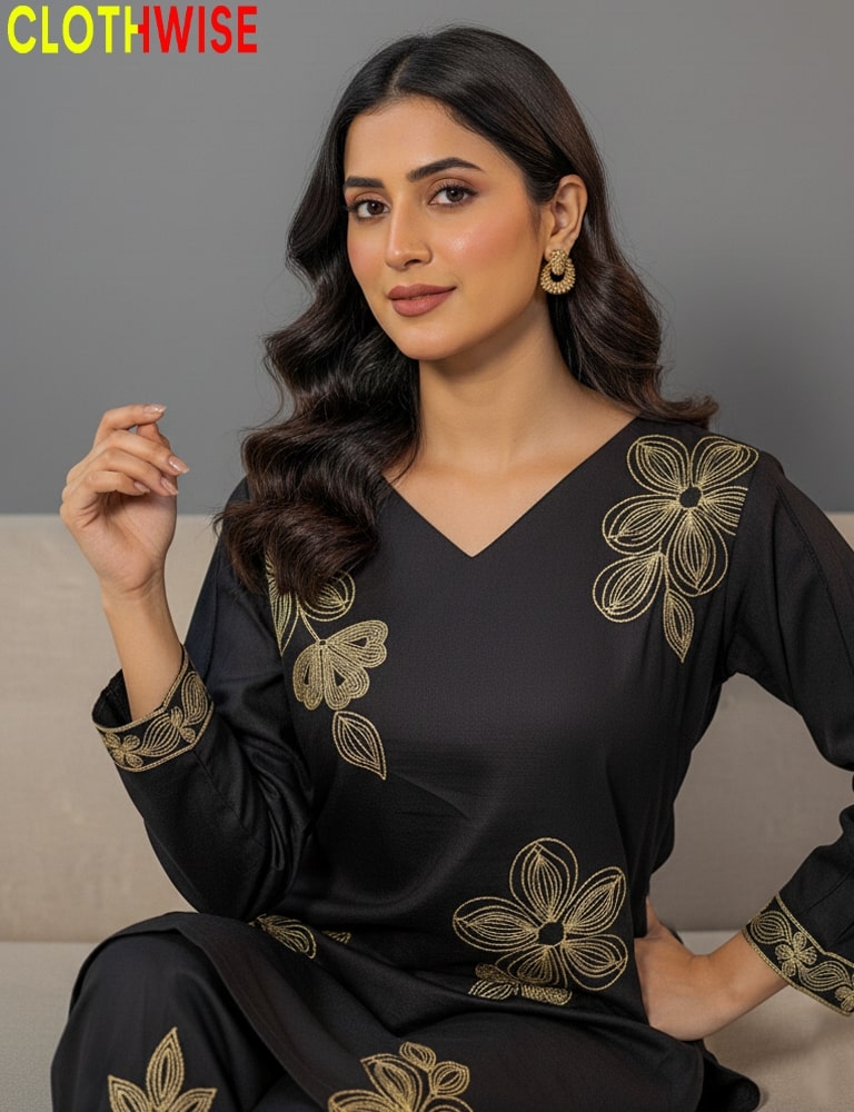 Woman wearing a black outfit with gold floral embroidery, sitting on a gray couch.