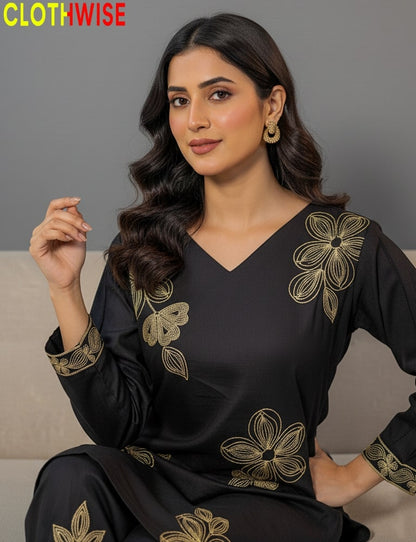 Woman wearing a black outfit with gold floral embroidery, sitting on a gray couch.