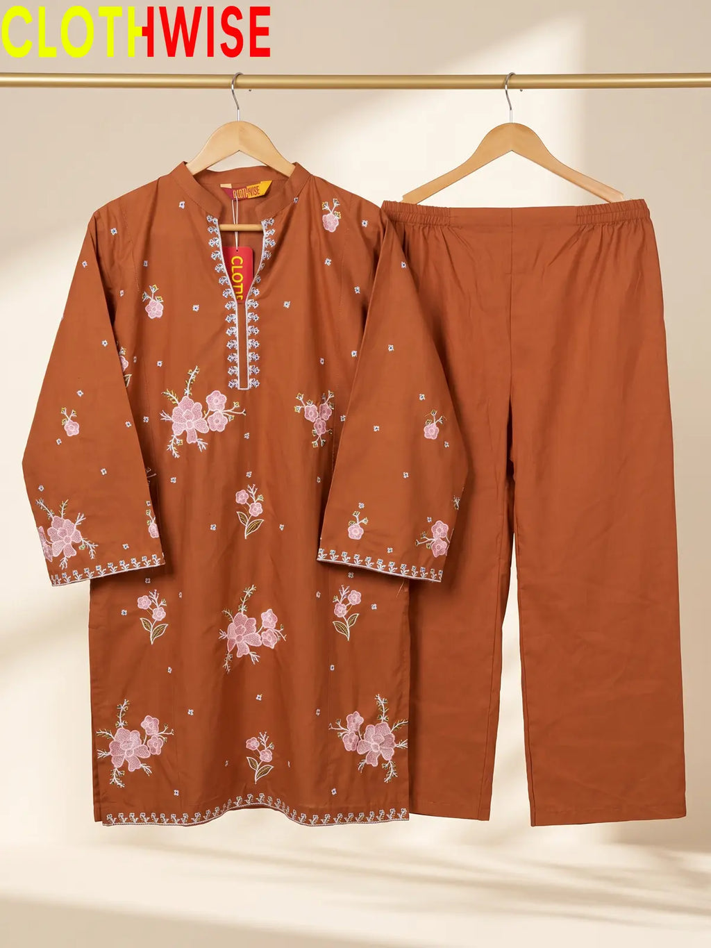 Hanger display of a rust 2-piece stitched outfit featuring a floral embroidered straight shirt and matching wide-leg trousers on a golden metal rack