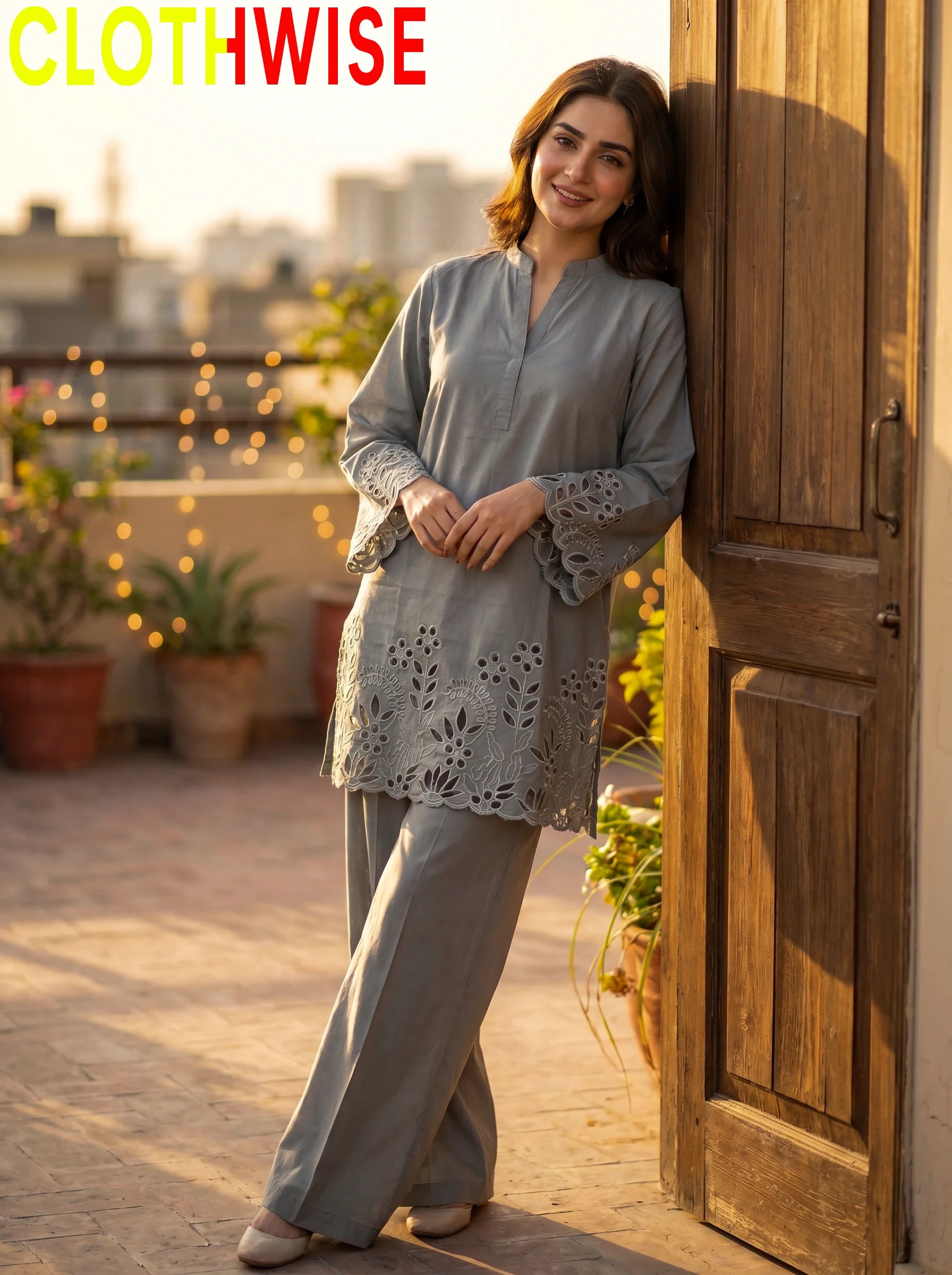 Woman in a light gray outfit standing on a rooftop with plants and cityscape in the background, featuring the brand 'CLOTHWISE'.