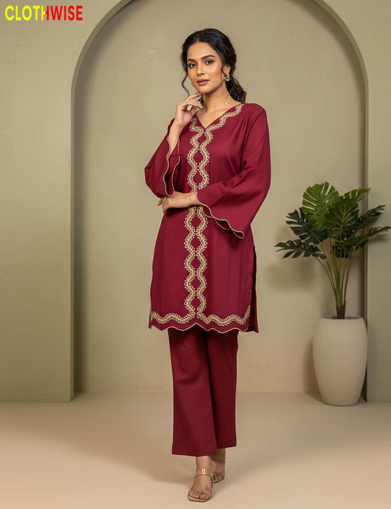 Woman wearing a maroon traditional outfit with intricate designs in a minimalistic setting.