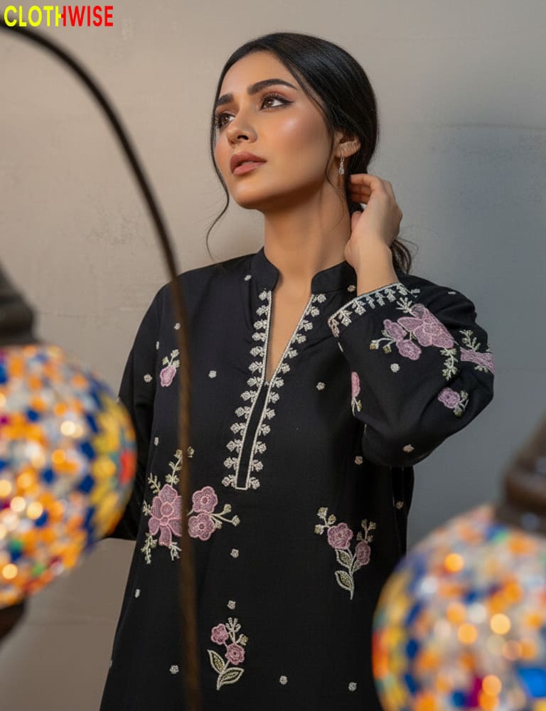 Woman wearing a black embroidered top with floral patterns, standing in front of colorful decorative items.