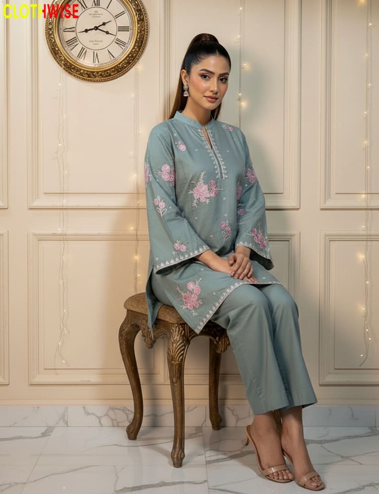 Woman in a light blue embroidered outfit sitting on a wooden stool with a clock and decorative lights in the background.
