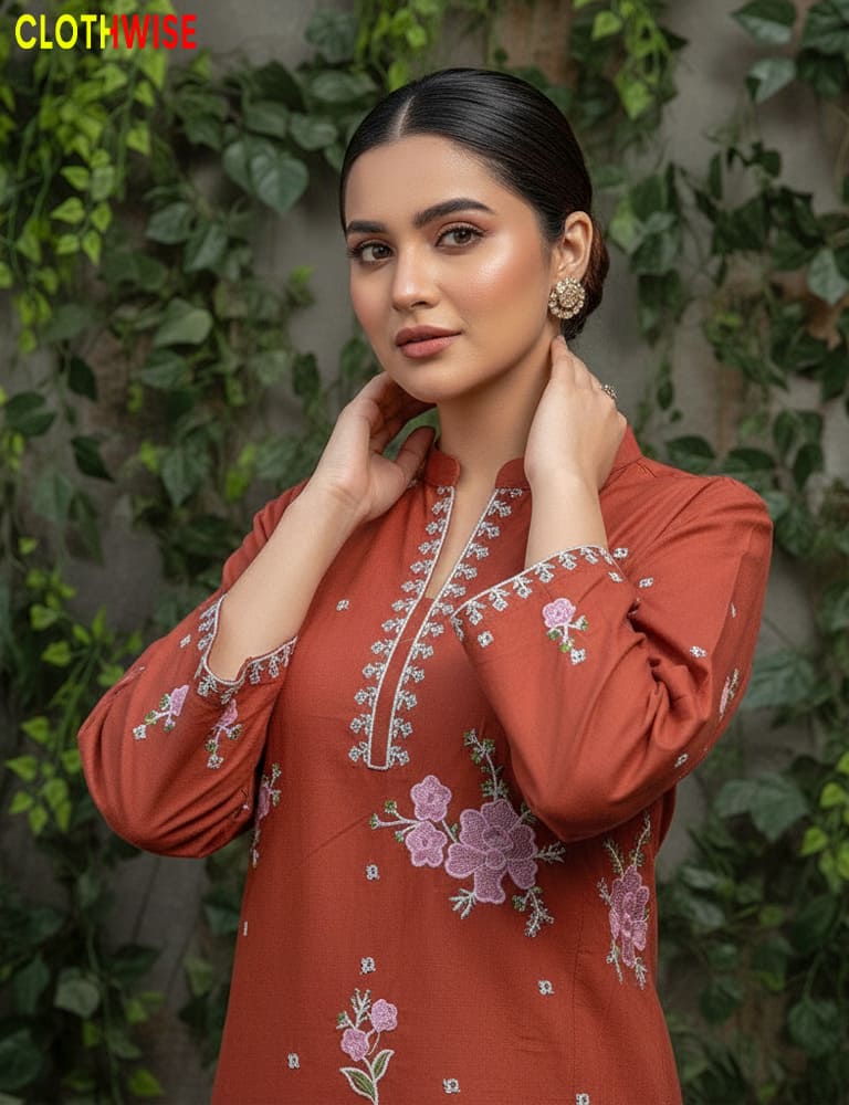 Woman wearing a rust-colored embroidered dress with floral patterns against a green leafy background.