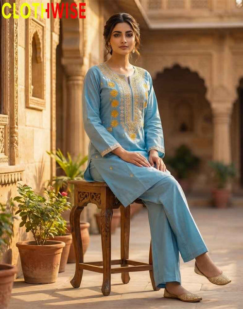 Woman in a light blue embroidered outfit sitting on a wooden stool in an outdoor setting with 'CLOTHWISE' branding.