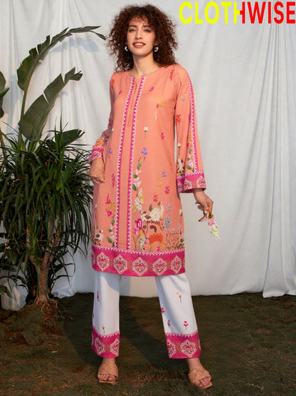 Woman wearing a peach embroidered top and white pants with pink borders, standing against a white curtain.