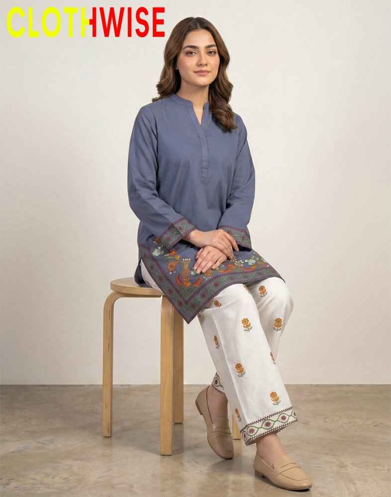 Woman sitting on a stool wearing a blue kurta with embroidery, white pants, and beige shoes against a plain background.