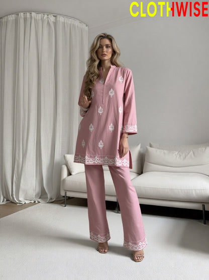 Woman wearing a pink outfit with white embroidery in a minimalistic room.