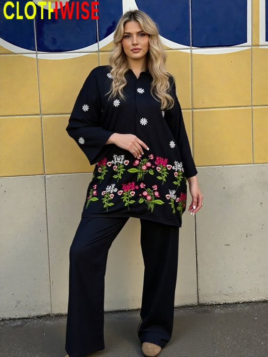 Woman wearing a black outfit with floral embroidery standing against a tiled wall.