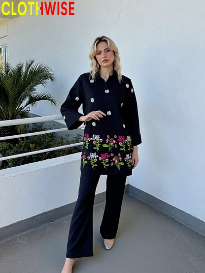Woman wearing a black outfit with floral embroidery standing on a balcony.