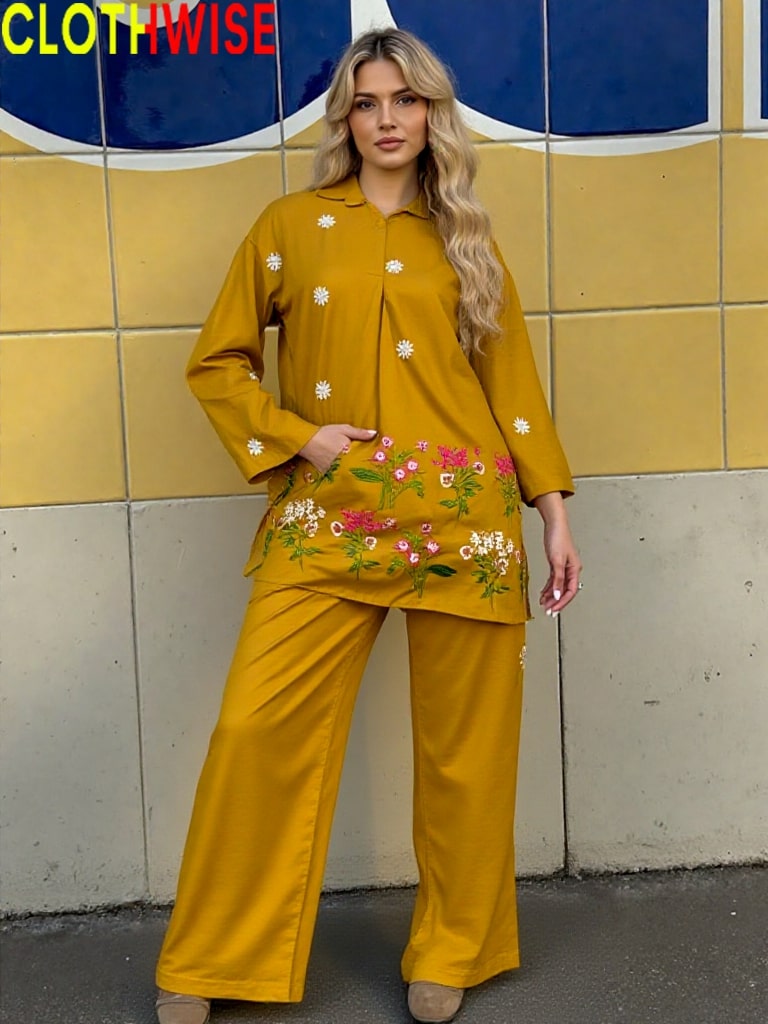 Woman wearing a mustard yellow outfit with floral patterns against a tiled wall.