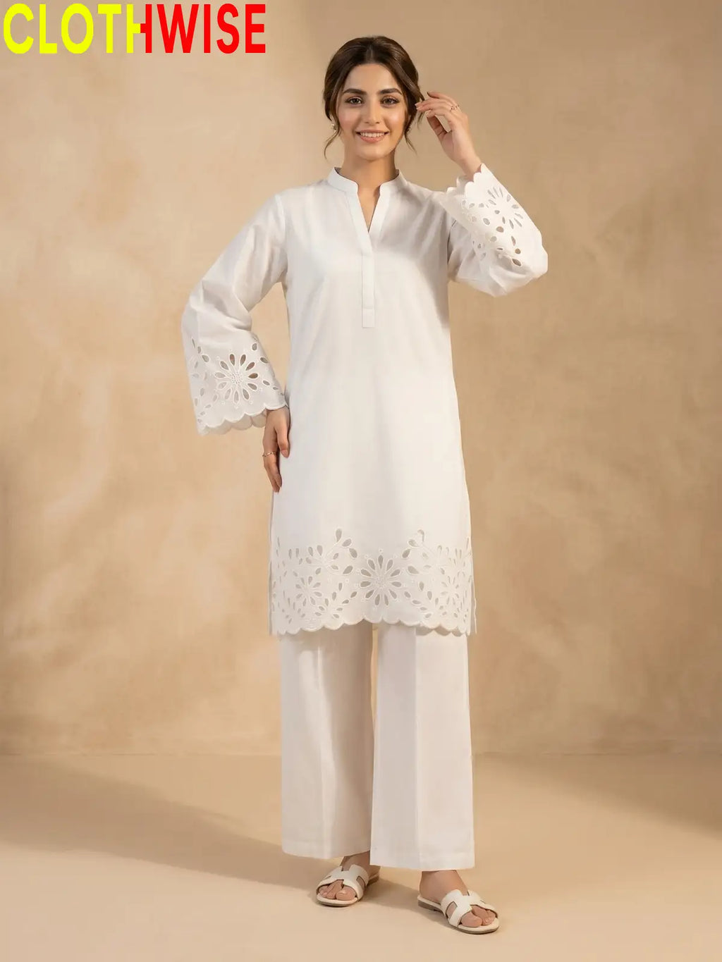 A woman modeling a white kurta and trouser set with eyelet lace detailing, standing against a warm beige textured backdrop. The brand name 'CLOTHWISE' is visible in the top left corner.